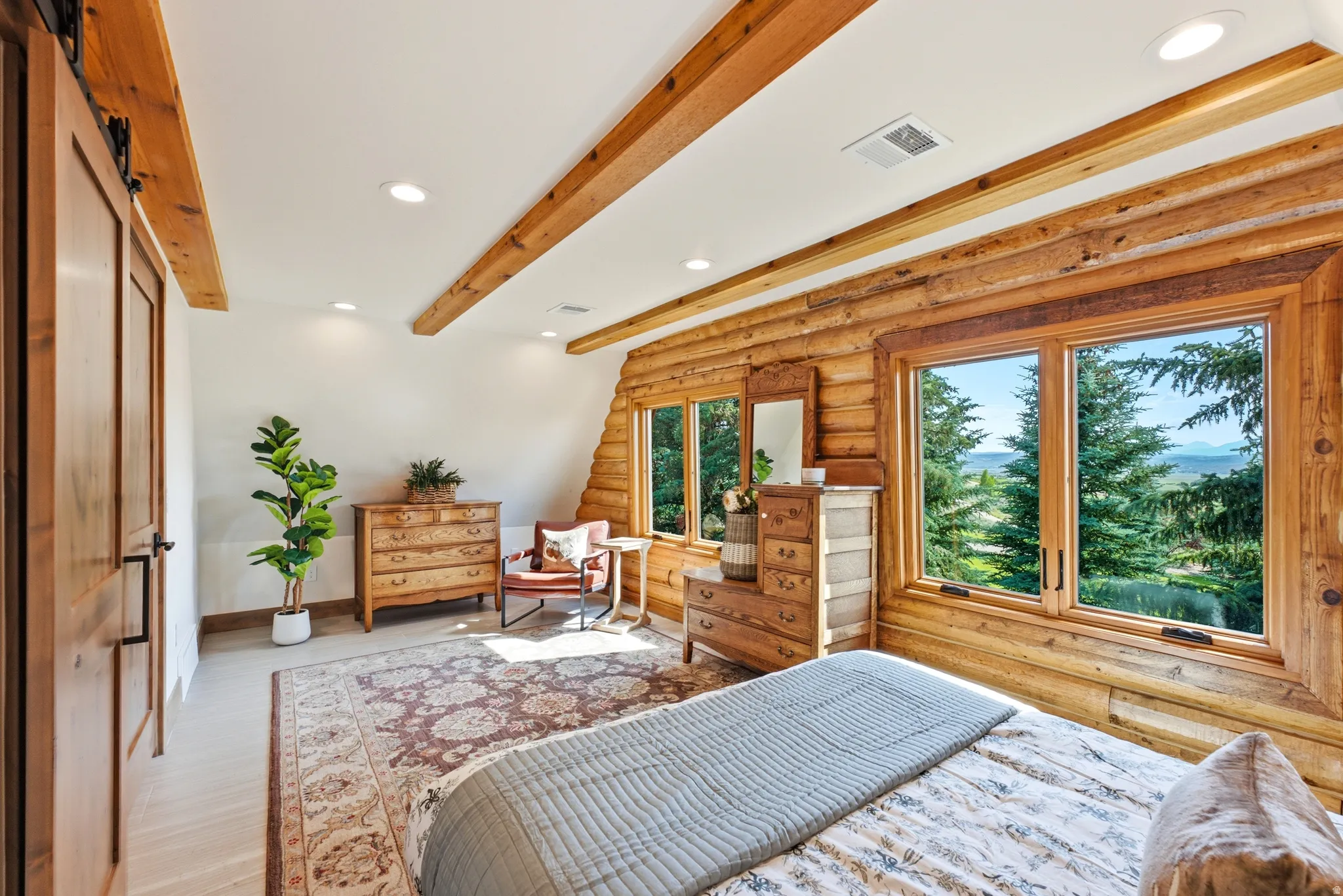 Expansive windows offering a scenic outdoor panorama, complemented by natural wood log walls and exposed ceiling beams