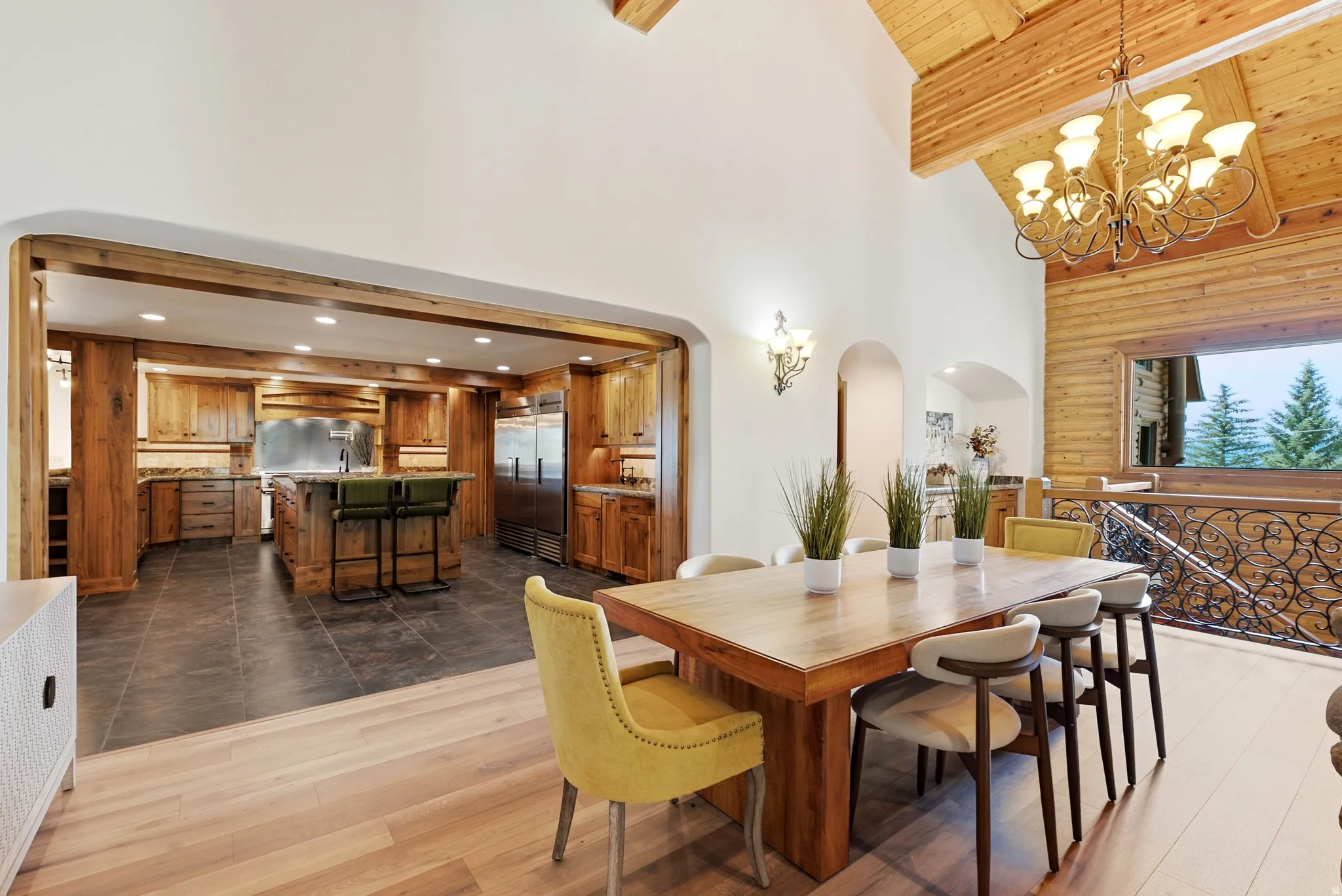 Open-concept dining area featuring wood-finish flooring, a vaulted wood-paneled ceiling with exposed beams, and an ornate chandelier