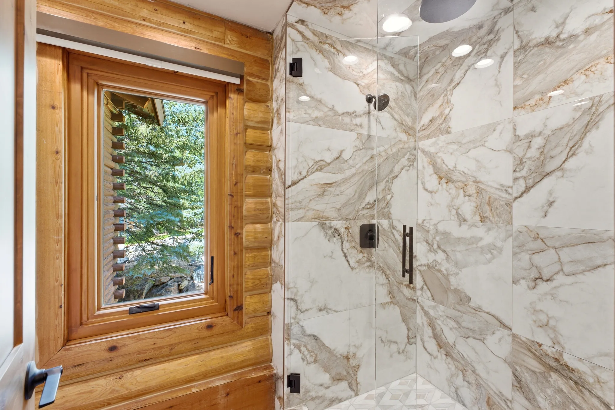 Glass-enclosed shower with large format marble-look tile walls and a rain shower head