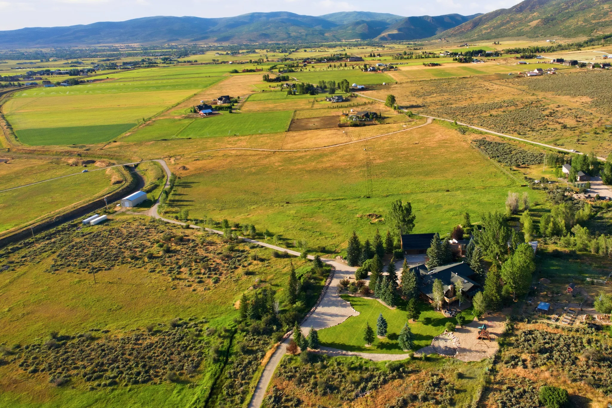 Expansive property featuring a central residence, mature trees, manicured lawns, and a winding driveway, all set against a backdrop of distant mountains and agricultural fields