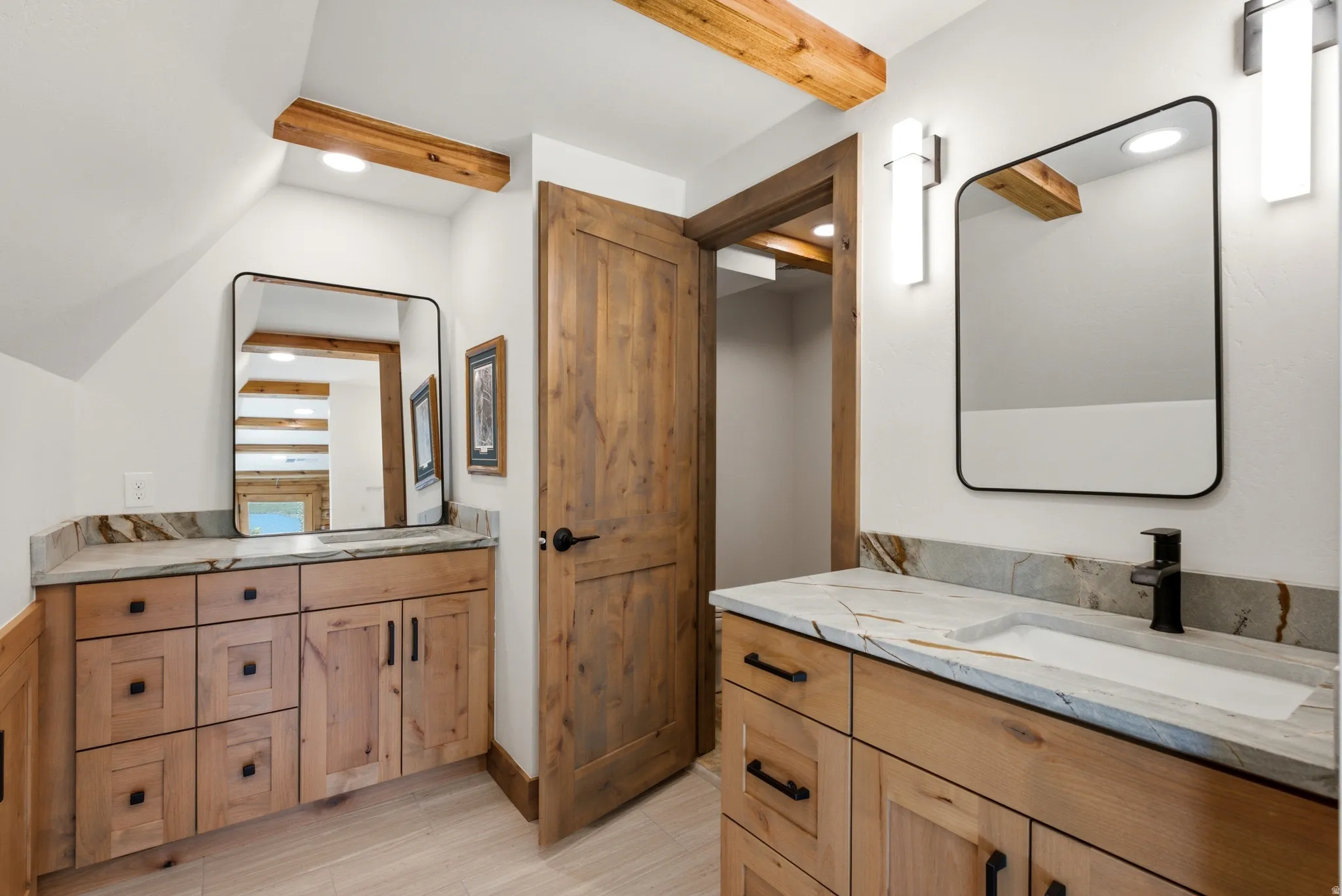 Dual vanity bathroom featuring light wood-finish cabinetry, stone countertops with integrated sinks, and contemporary wall-mounted light fixtures