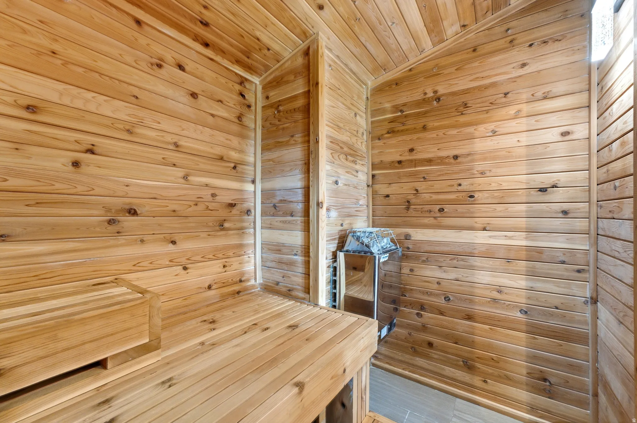 Interior sauna featuring horizontal wood paneling, a built-in wood bench, a wall-mounted sauna heater, and a tiled floor
