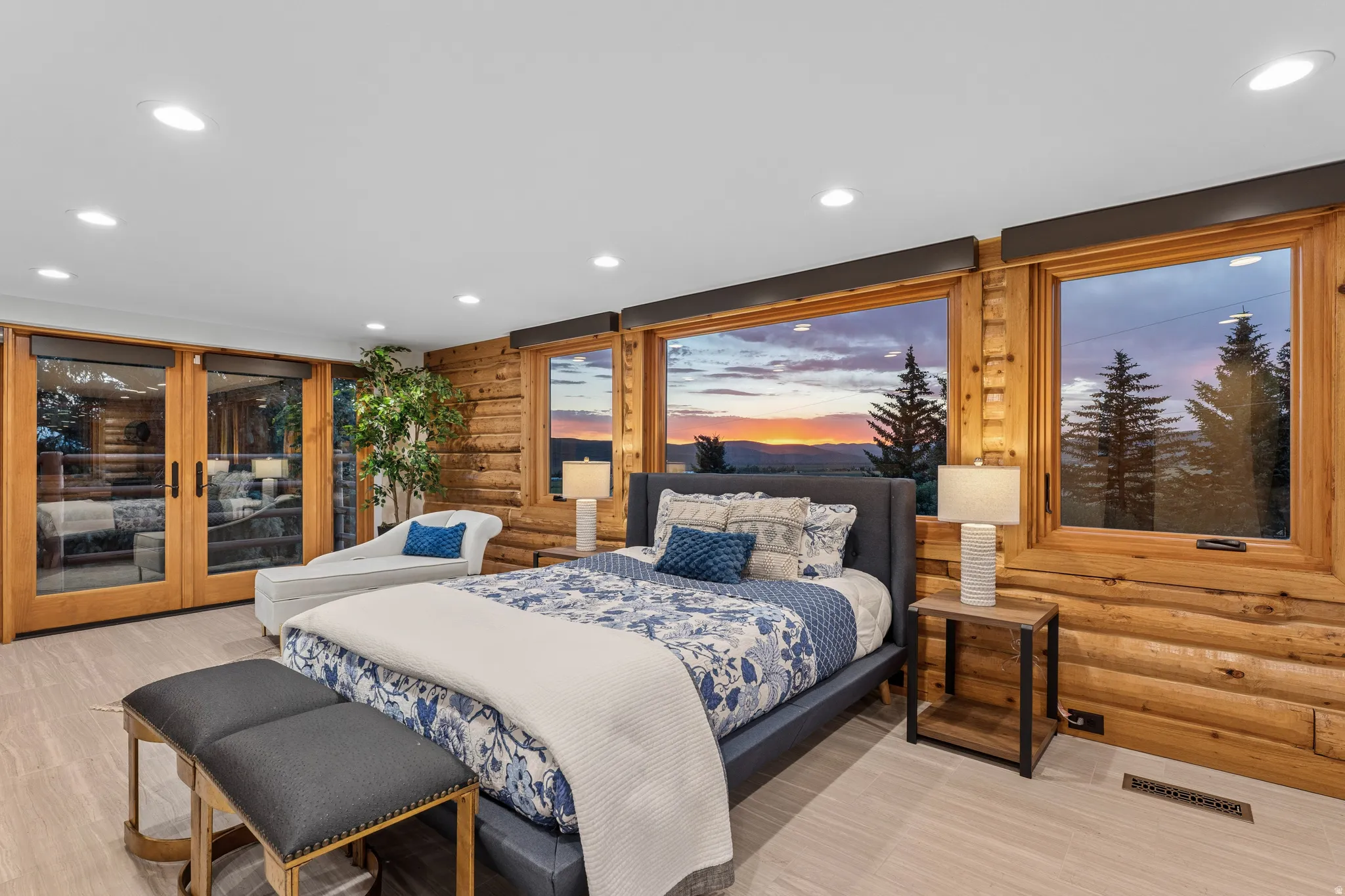 Bedroom featuring log wall construction, light wood-finish flooring, recessed ceiling lighting, and large windows with outdoor scenery