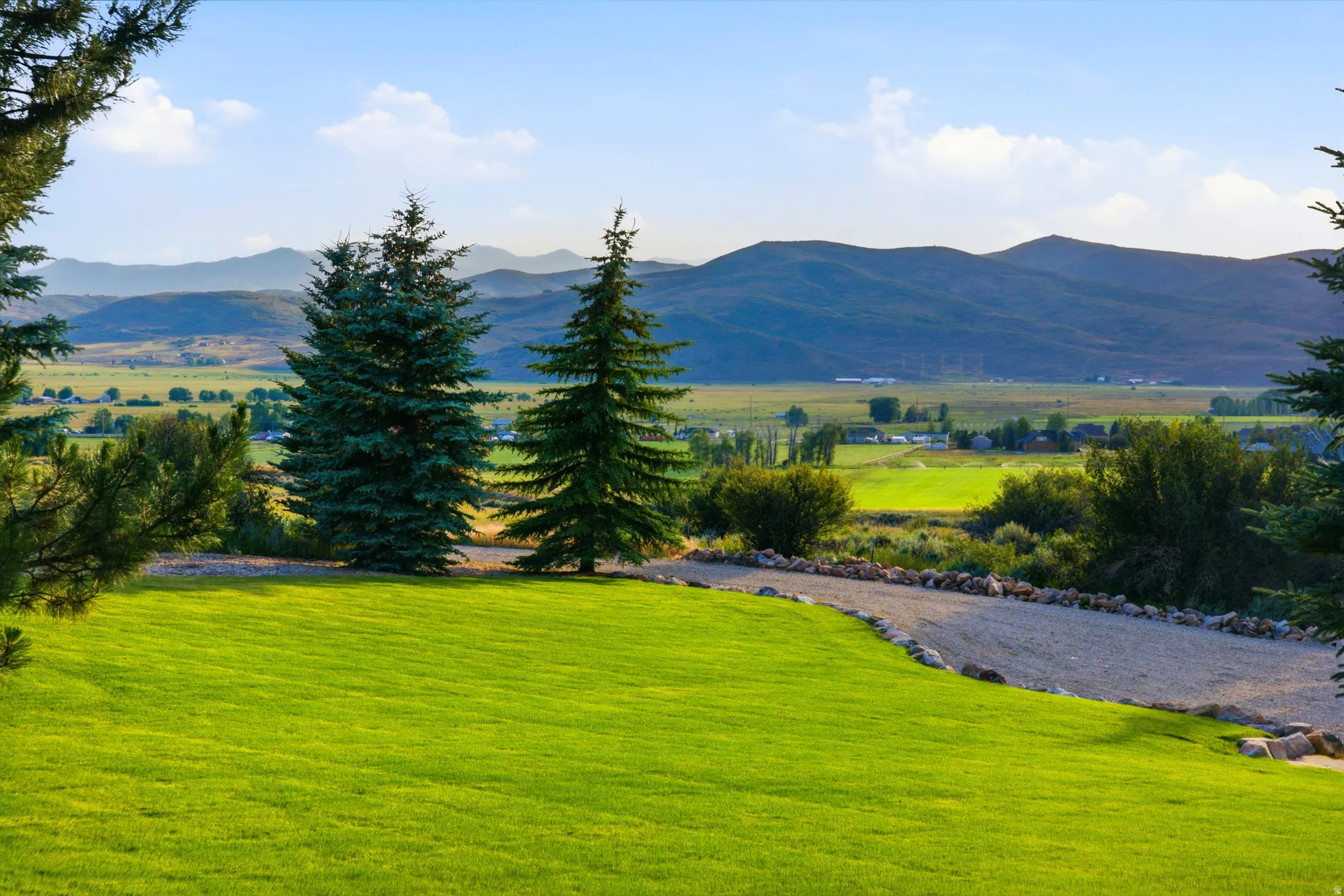 Expansive green lawn with mature evergreen trees, a gravel pathway, and distant mountain scenery