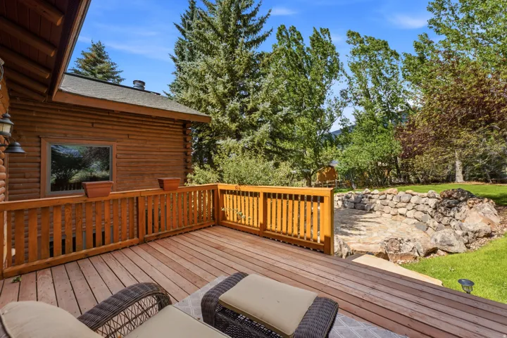 Expansive wood-finish deck with a wooden railing system, featuring an exterior log-finish wall, and a stone-lined patio area