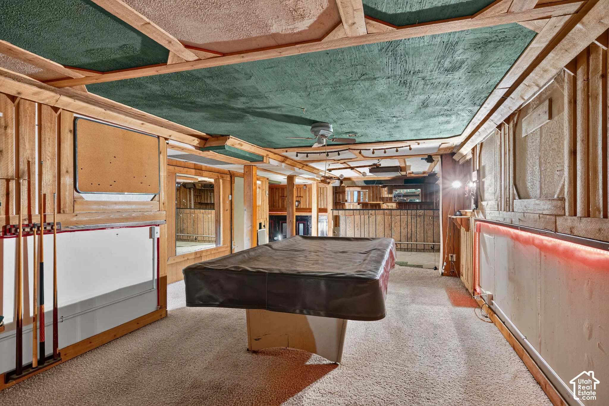 Finished basement featuring natural wood wall paneling, a painted textured ceiling with exposed wooden framing, carpeted flooring, and integrated linear lighting