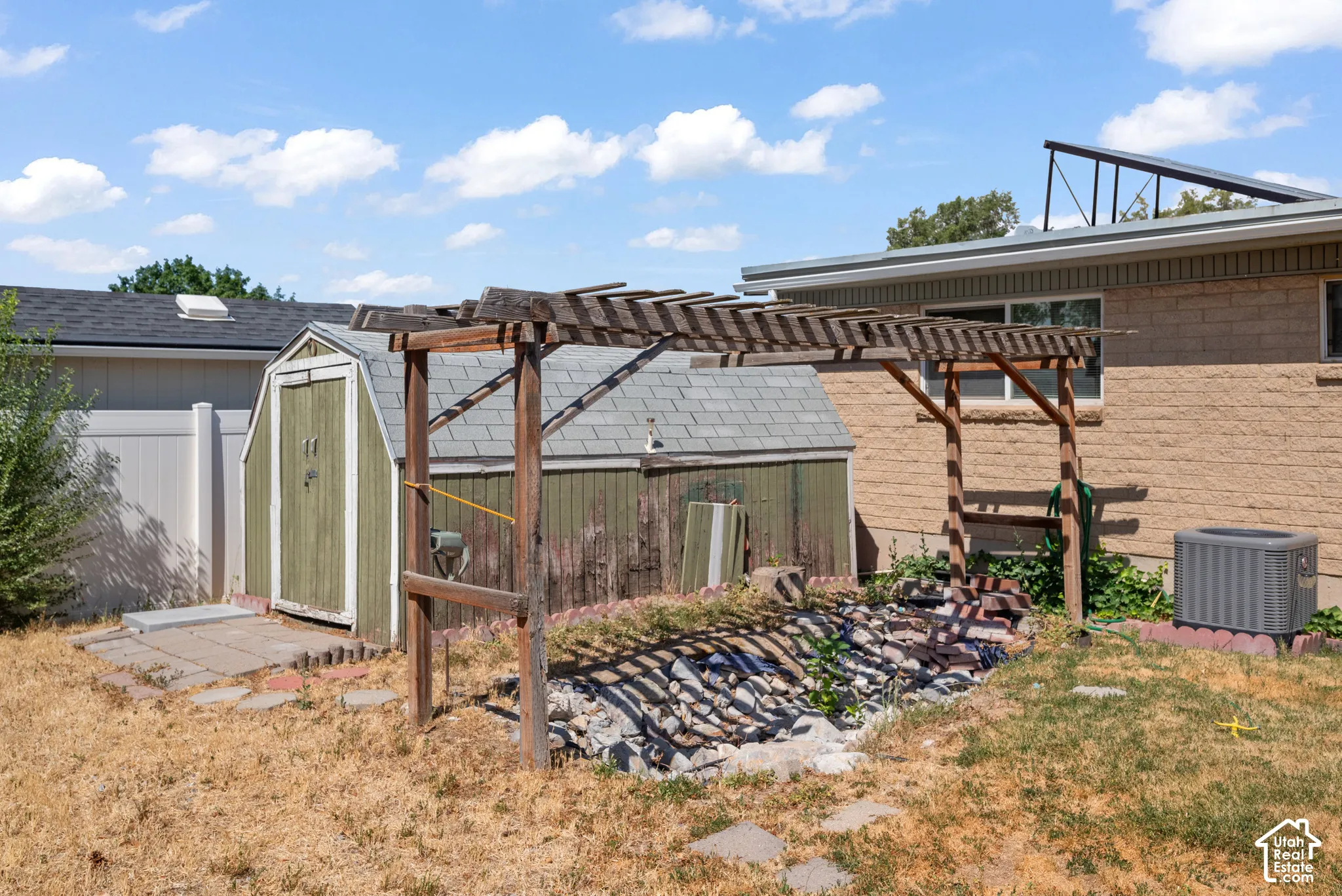 Backyard featuring a wooden pergola, stone-filled garden bed, detached storage shed, masonry exterior, and vinyl privacy fencing