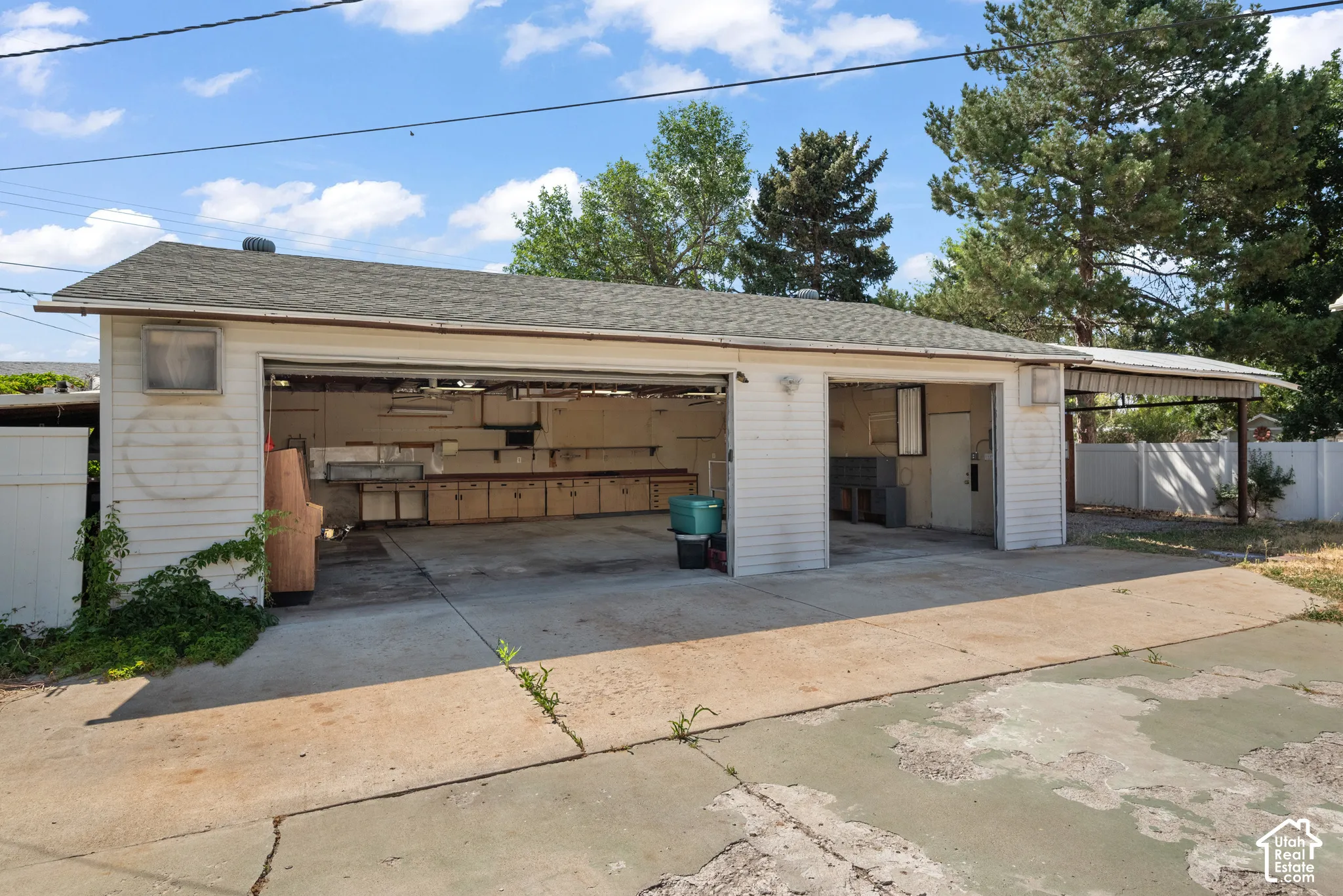 Detached two-car garage featuring horizontal siding, a composite shingle roof, integrated workshop cabinetry, and an attached side carport