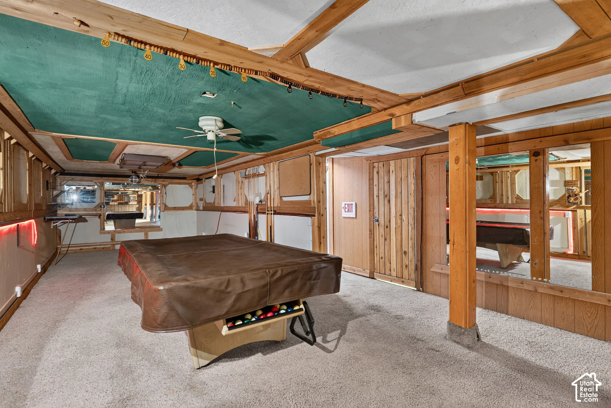 Wood-paneled walls, decorative coffered ceiling with green fabric accents, ceiling fan, and structural support column