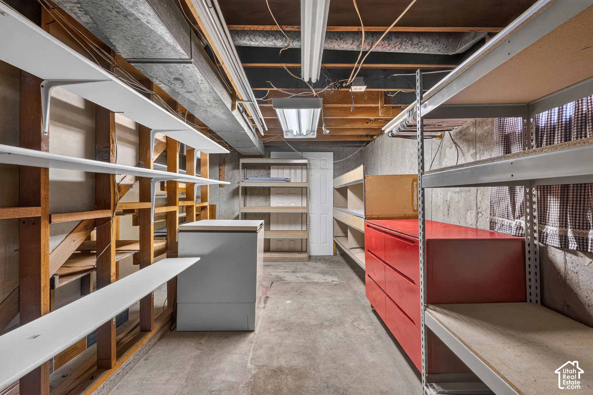 Utility storage space featuring exposed ceiling joists, concrete foundation walls, concrete flooring, and multiple tiers of built-in shelving