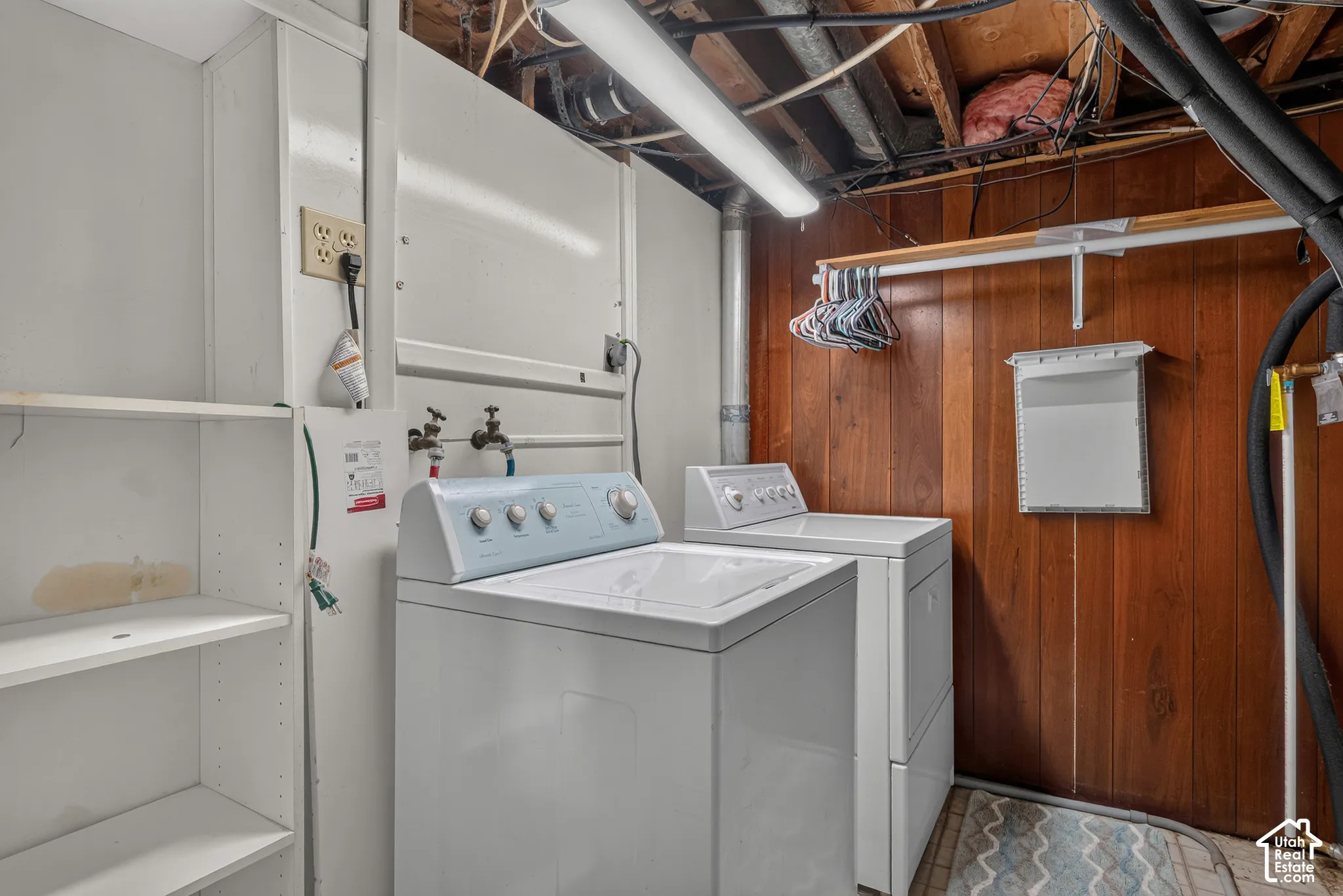 Laundry area featuring wood-paneled walls, built-in shelving, and mounted garment storage