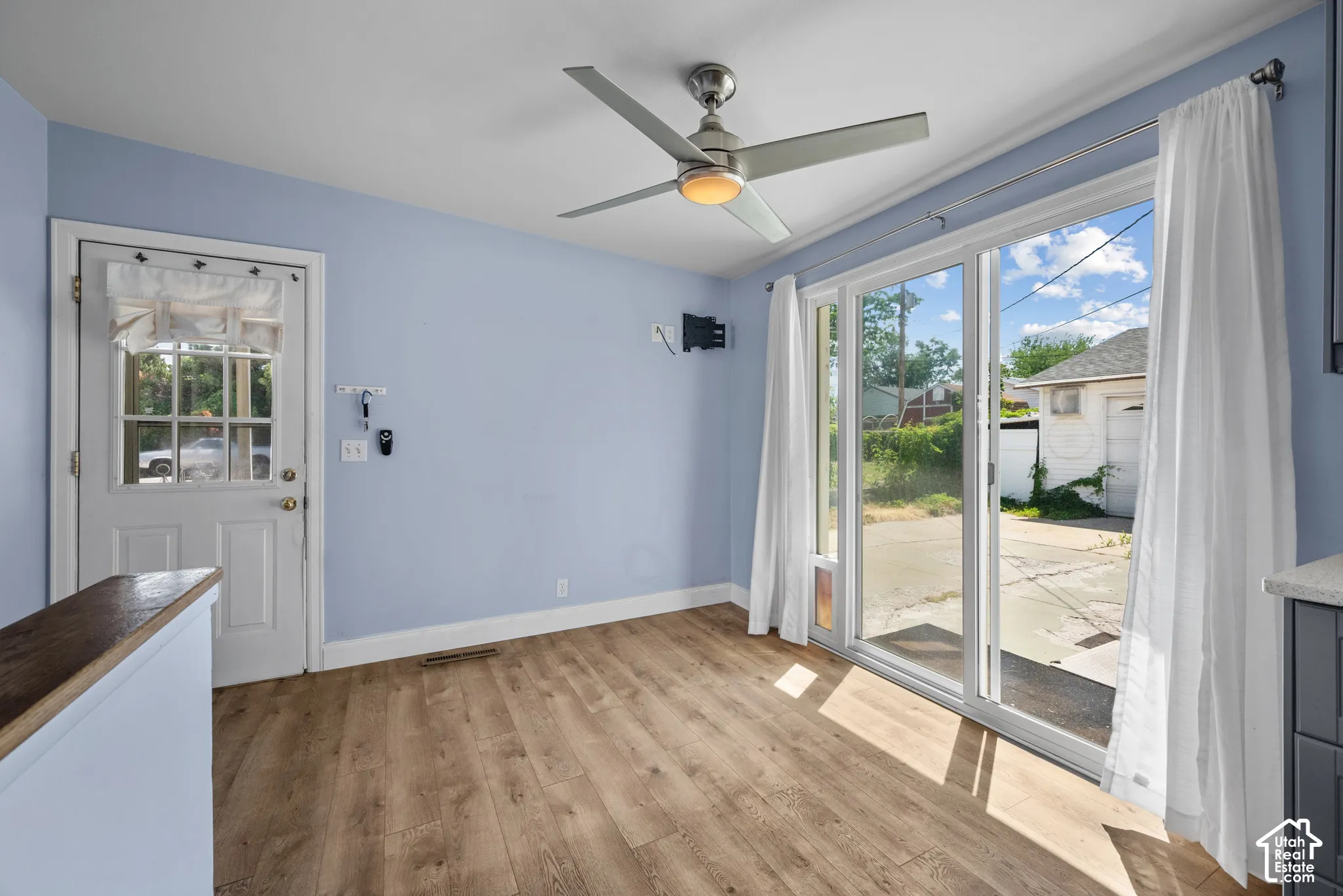 Room featuring wood-finish flooring, a contemporary ceiling fan, a glass-paneled exterior door, and a sliding glass door