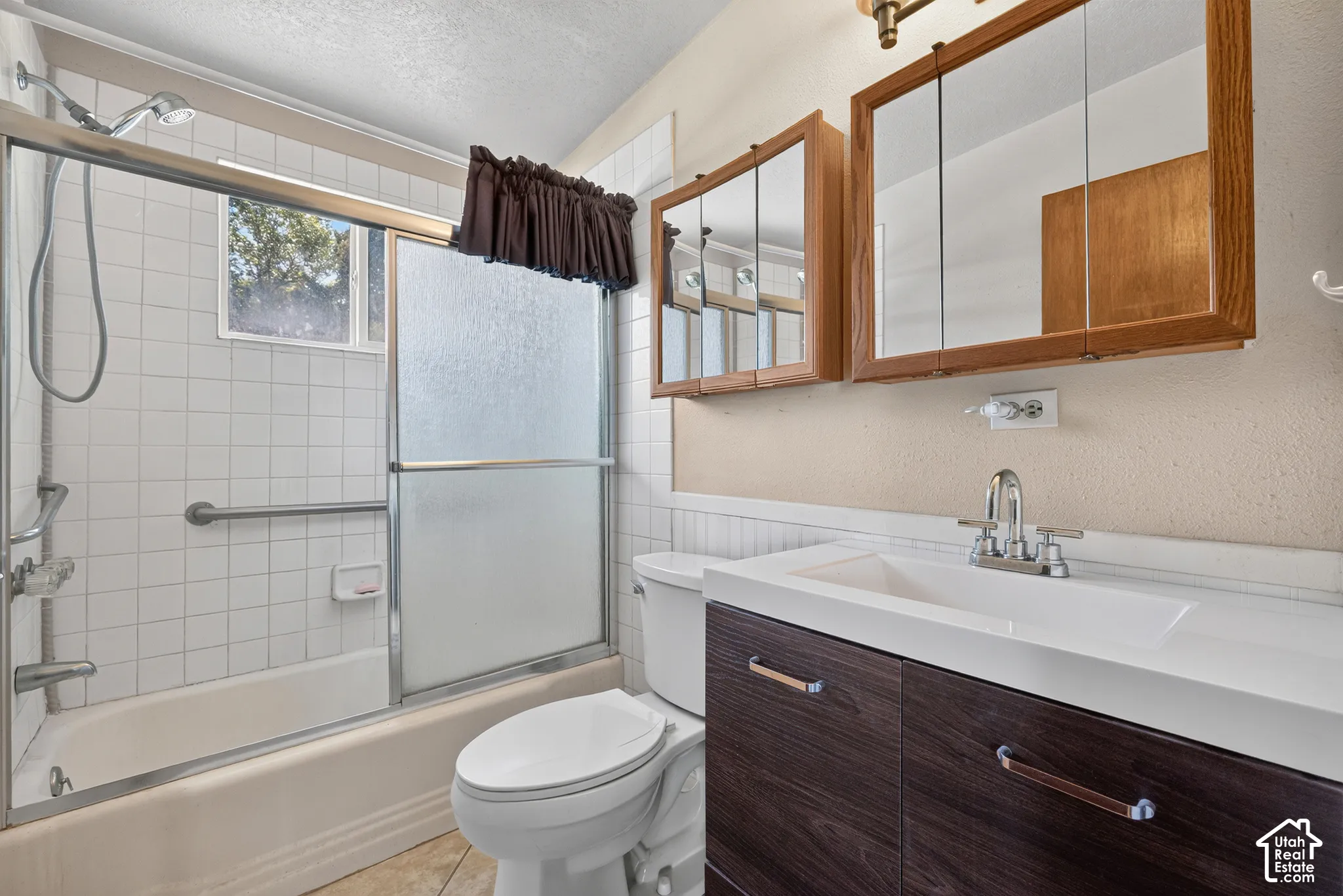 Bathroom featuring a dark wood-finish vanity with an integrated rectangular sink, dual mirrored medicine cabinets, and a tub-shower combination with sliding glass doors and wall-mounted grab bars