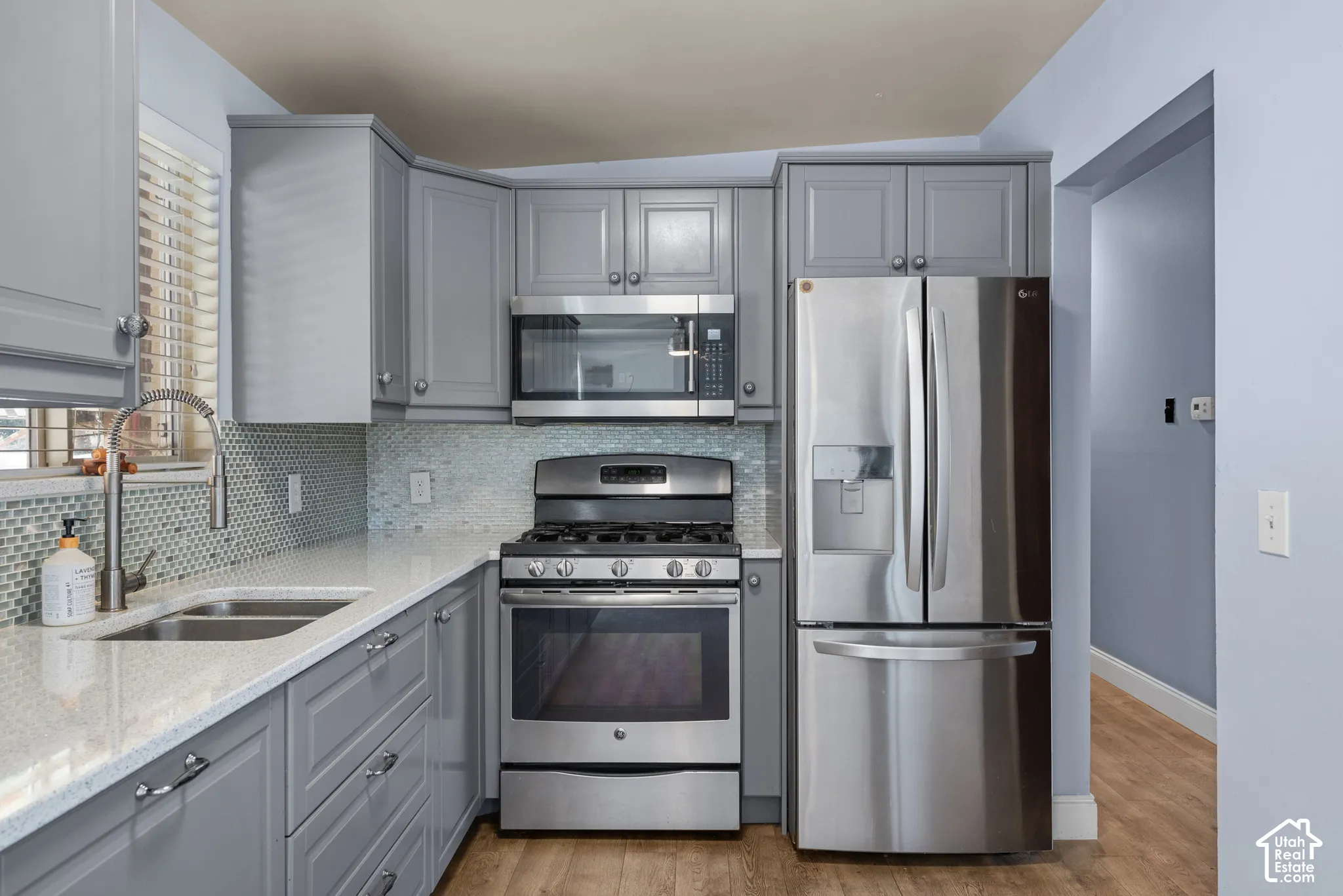 Kitchen featuring grey cabinetry, stainless steel appliances, quartz countertops, a mosaic tile backsplash, and a high-arch gooseneck faucet