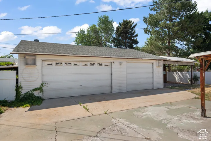 Detached two-car garage featuring shingled roof, horizontal siding, and additional covered parking structure
