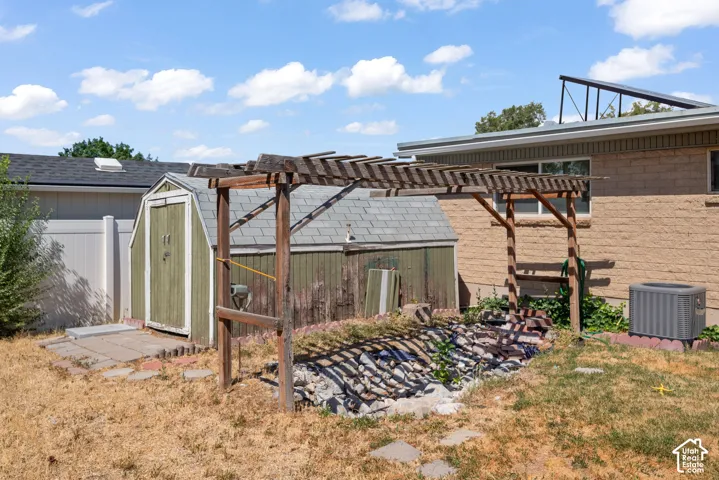 Backyard featuring a wooden pergola, stone-filled garden bed, detached storage shed, masonry exterior, and vinyl privacy fencing