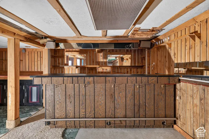 Custom built-in wood bar featuring a dark countertop, vertical wood paneling, an integrated metal foot rail, and mirrored back shelving