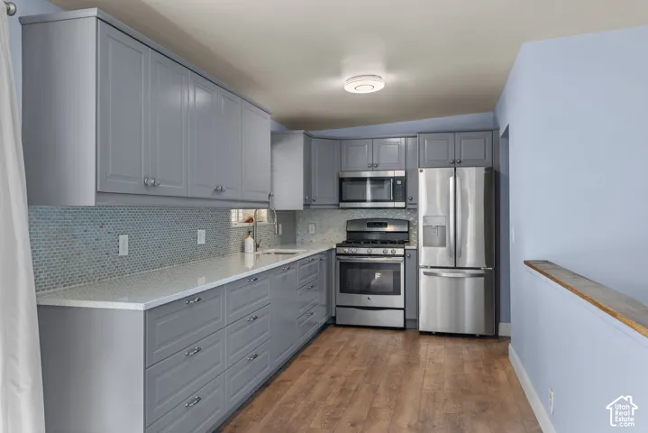 Kitchen featuring gray shaker-style cabinetry, white countertops, mosaic tile backsplash, stainless steel appliances, and wood-finish flooring