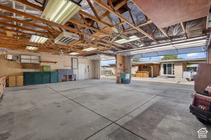 Spacious garage featuring exposed wood truss ceiling, concrete flooring, overhead fluorescent lighting, and multiple wall-mounted electrical outlets