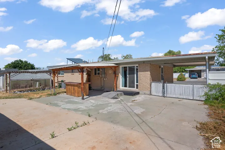 Brick exterior featuring a concrete patio, wood-frame pergola, attached carport, and chain-link fencing
