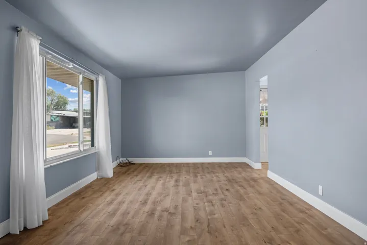 Spacious room featuring wood-finish flooring, light blue wall tones, white baseboards, and a large multi-pane window