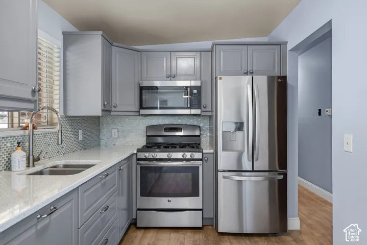 Kitchen featuring grey cabinetry, stainless steel appliances, quartz countertops, a mosaic tile backsplash, and a high-arch gooseneck faucet