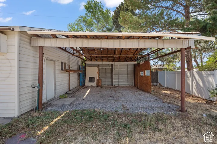 Covered carport with a gravel surface, metal support columns, and white privacy fencing