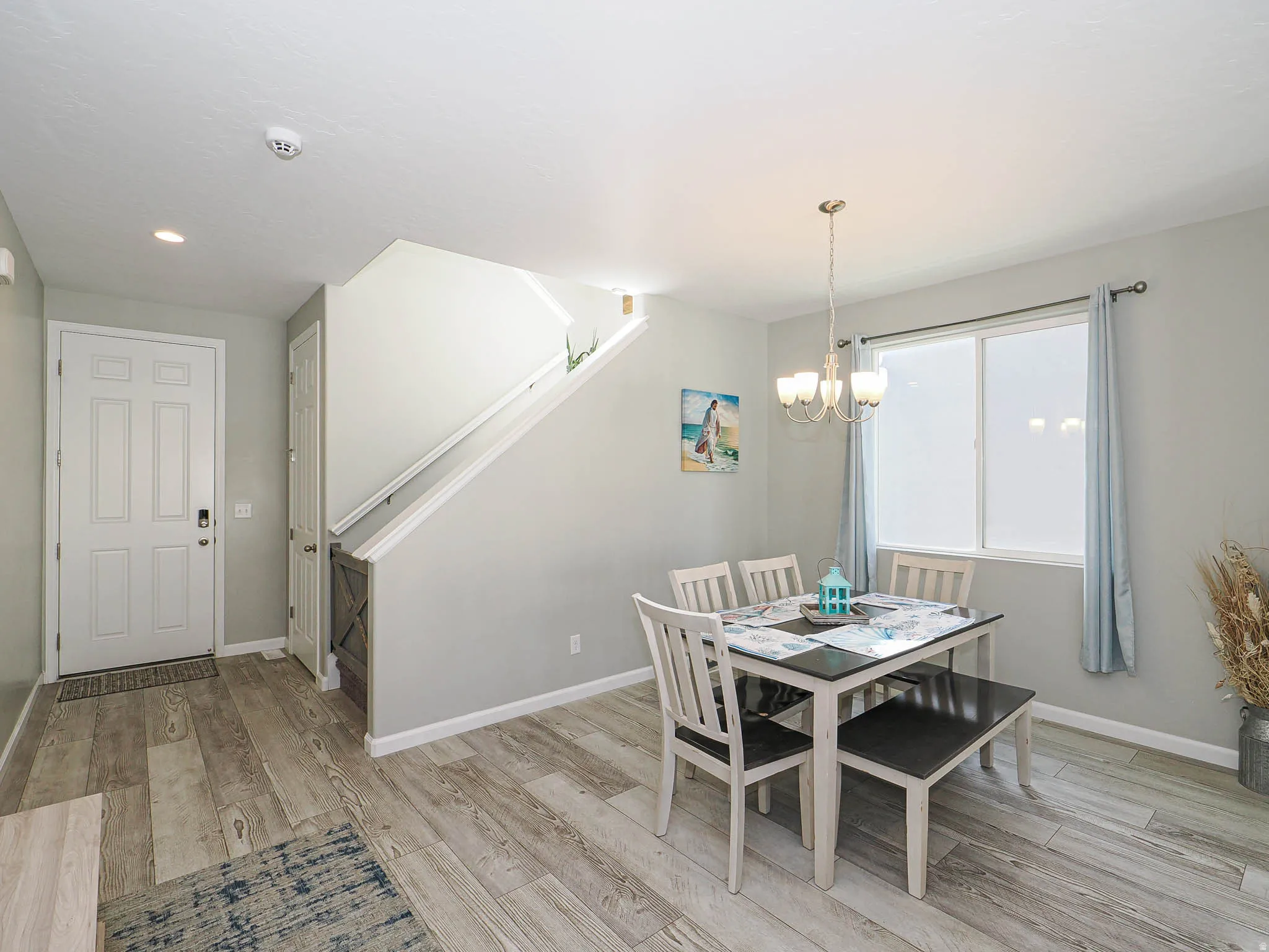 Entryway and dining area featuring wood-finish flooring, a white paneled front door, and a staircase with a wood railing
