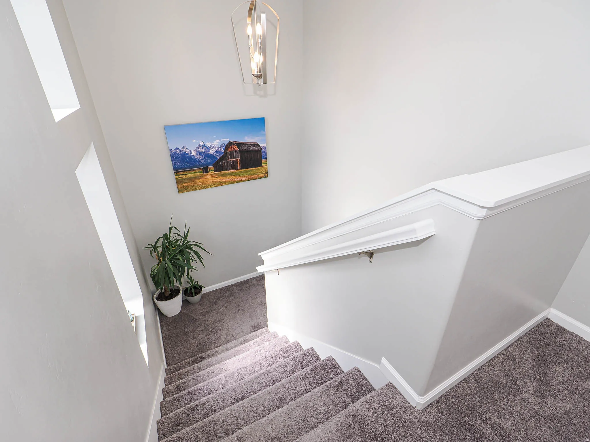 Carpeted staircase with white trim, featuring a contemporary pendant light fixture and a handrail