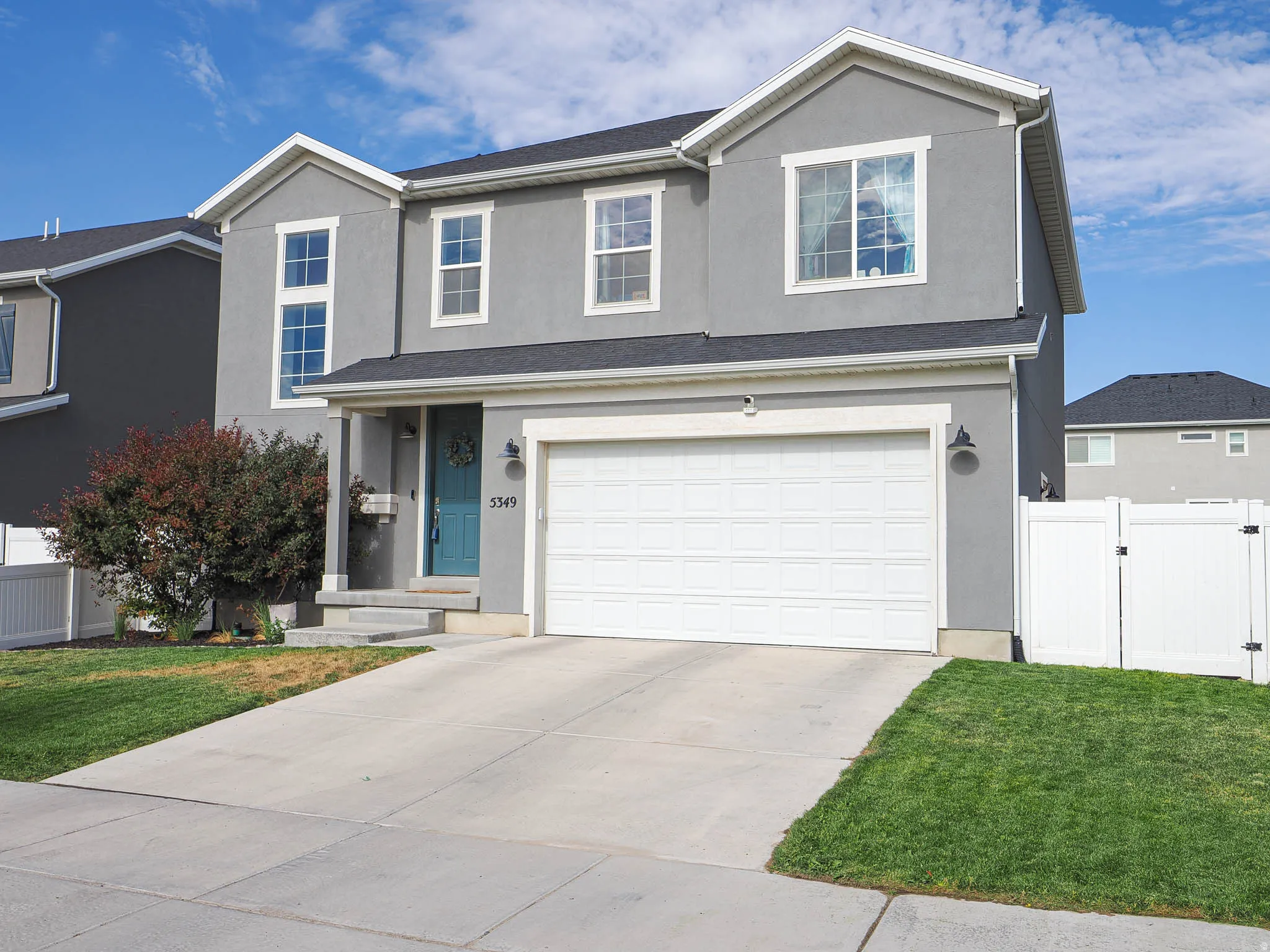 Contemporary two-story exterior with a two-car garage, gray stucco siding, and a vibrant teal front door