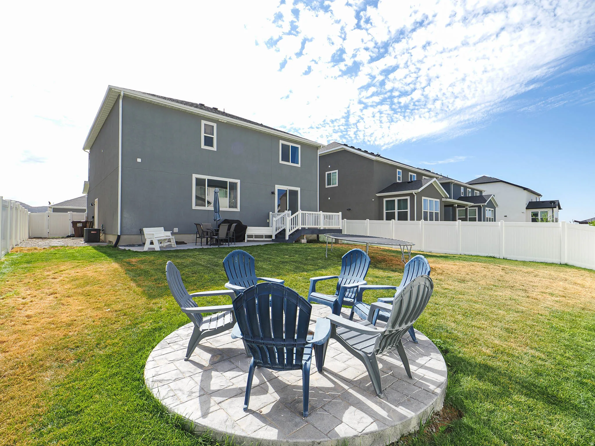 Expansive backyard featuring a circular paver patio, a white vinyl privacy fence, and a two-story exterior with multiple windows