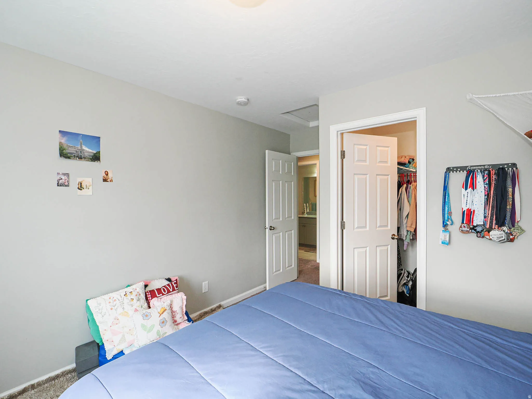 Neutral wall paint in a bedroom featuring two white paneled doors, one leading to a closet with shelving and the other to a full bathroom with a vanity