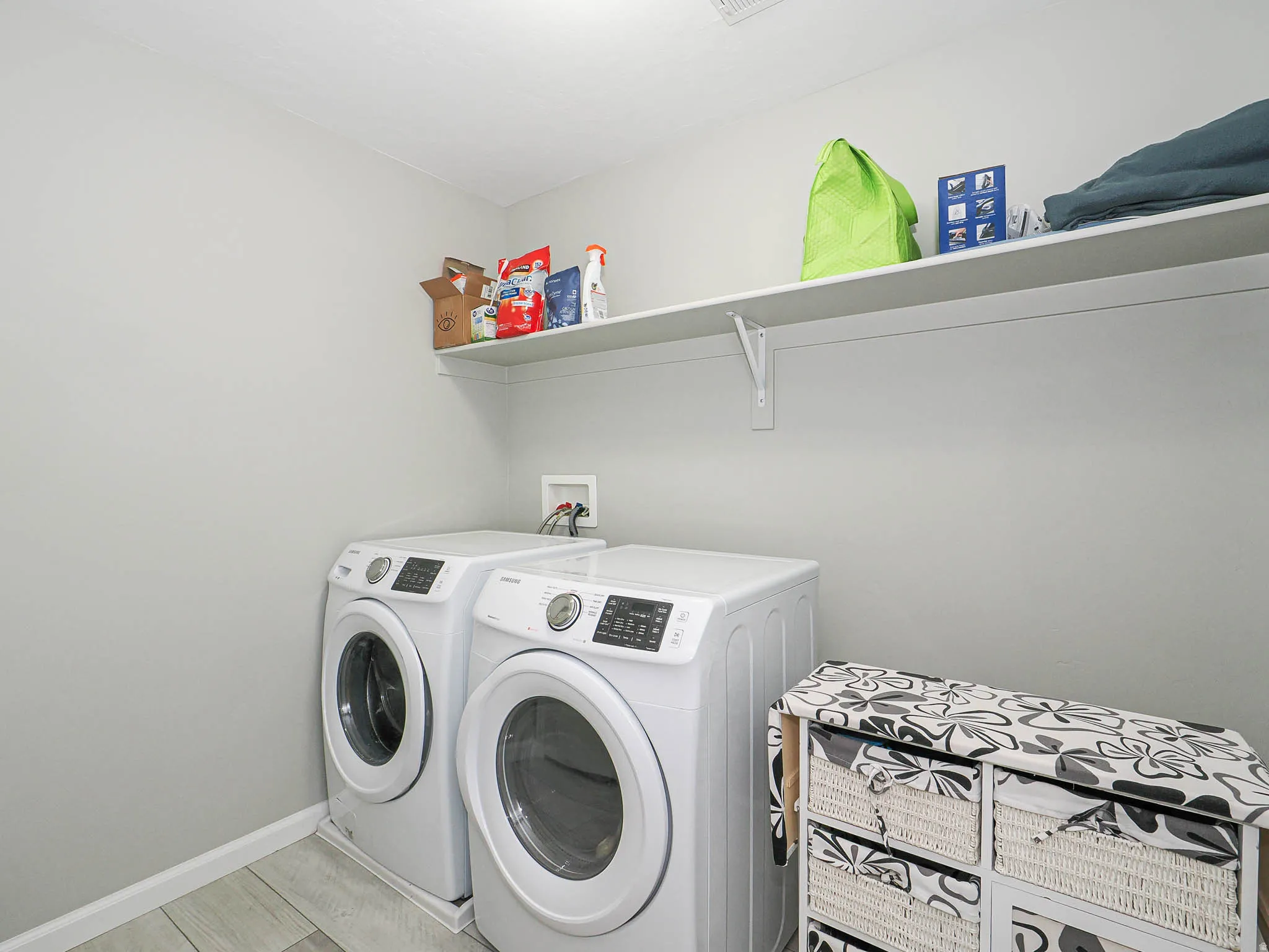 Laundry area featuring light gray walls, wood-finish flooring, and a wall-mounted storage shelf