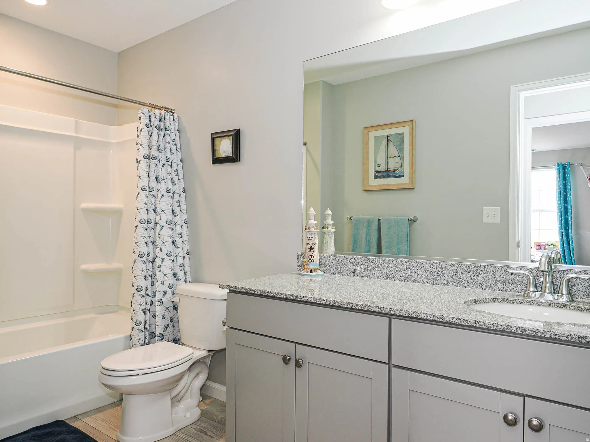 Bathroom featuring a white tub with integrated shower, light gray cabinetry, and a granite-finish countertop with an integrated sink