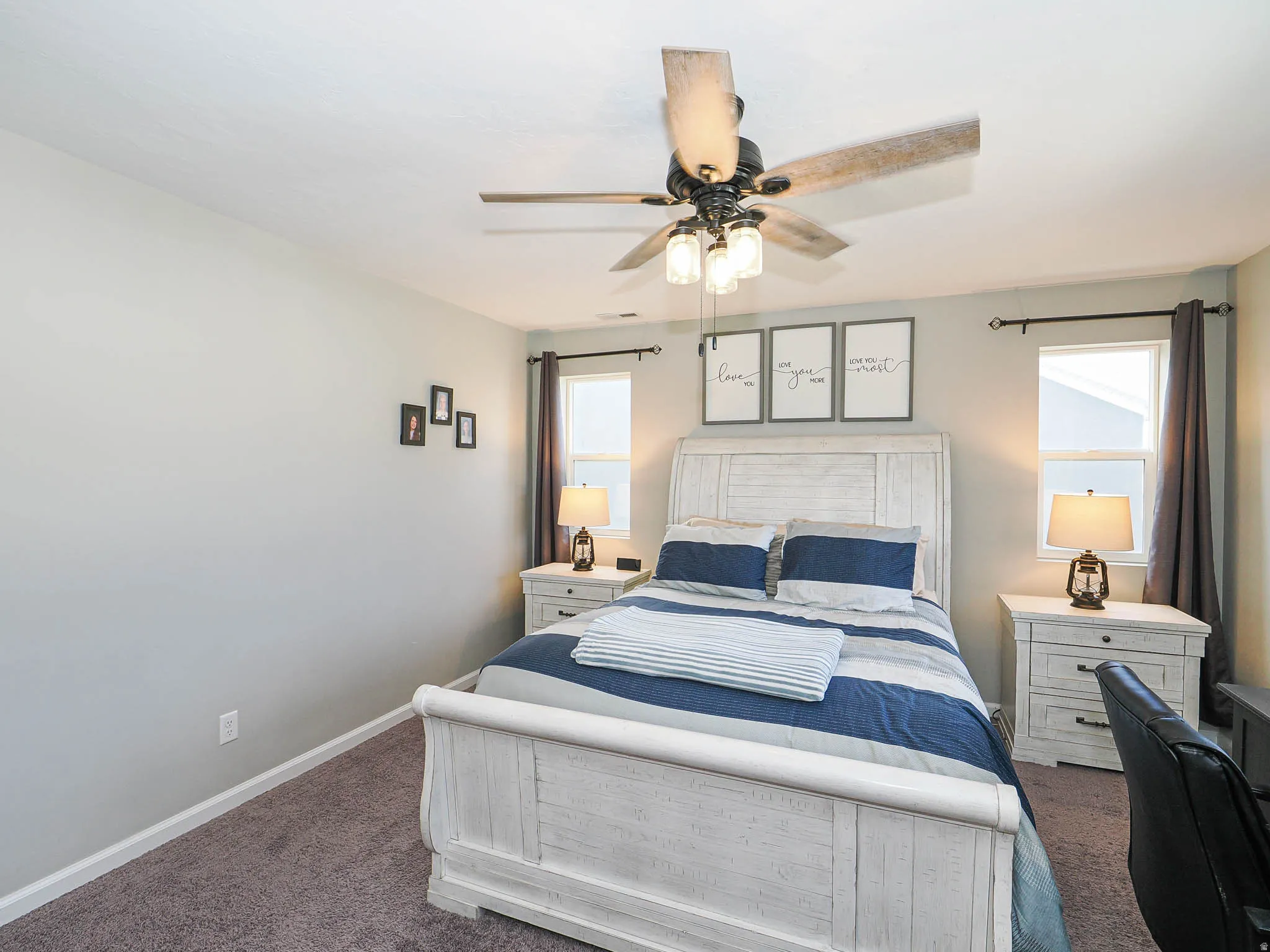 Bedroom featuring a ceiling fan with light kit, two windows with curtain rods, and neutral-toned walls