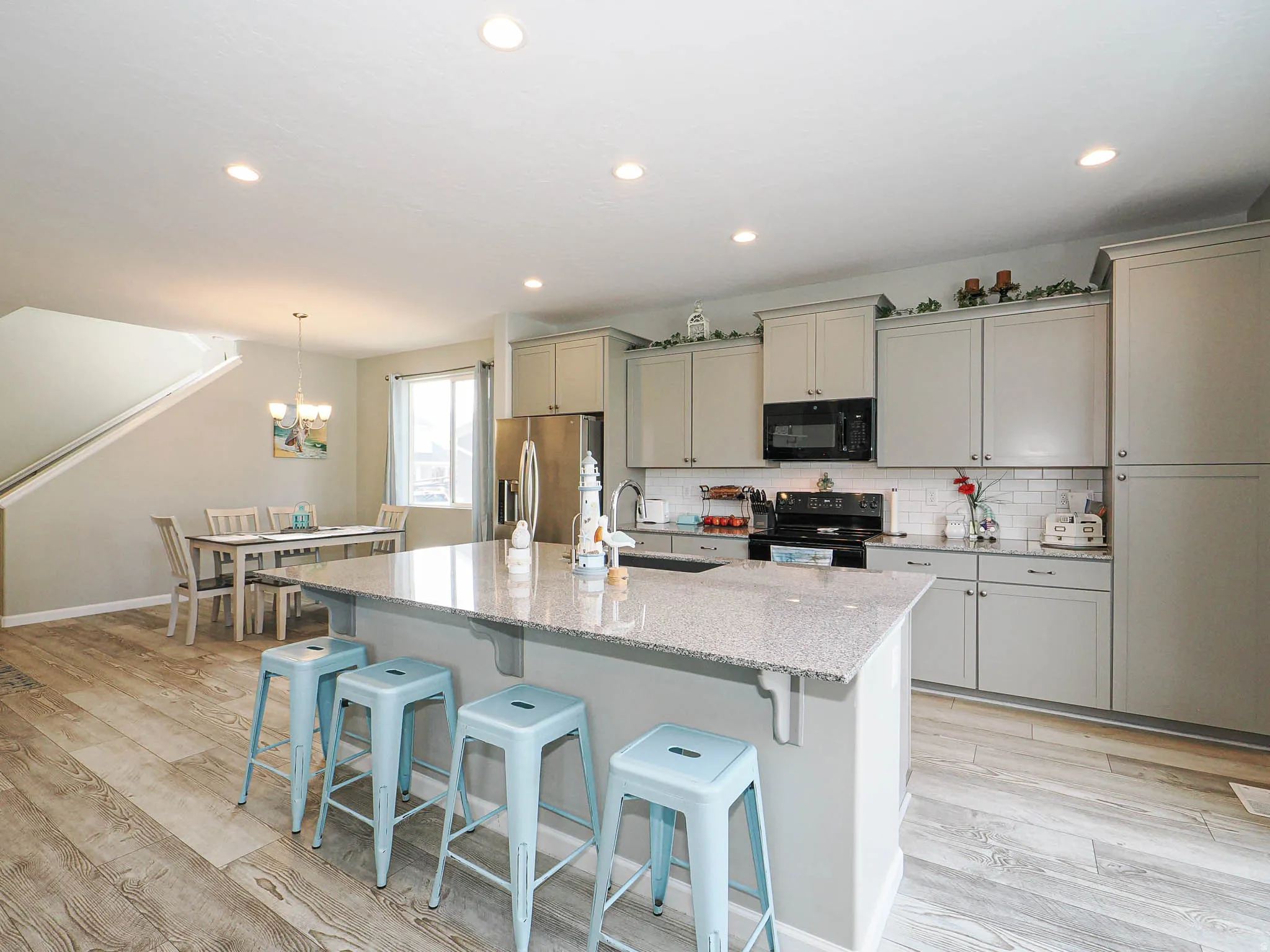 Open-concept kitchen featuring an island with a light-colored countertop, light gray cabinetry, stainless steel refrigerator, black range, and wood-finish flooring