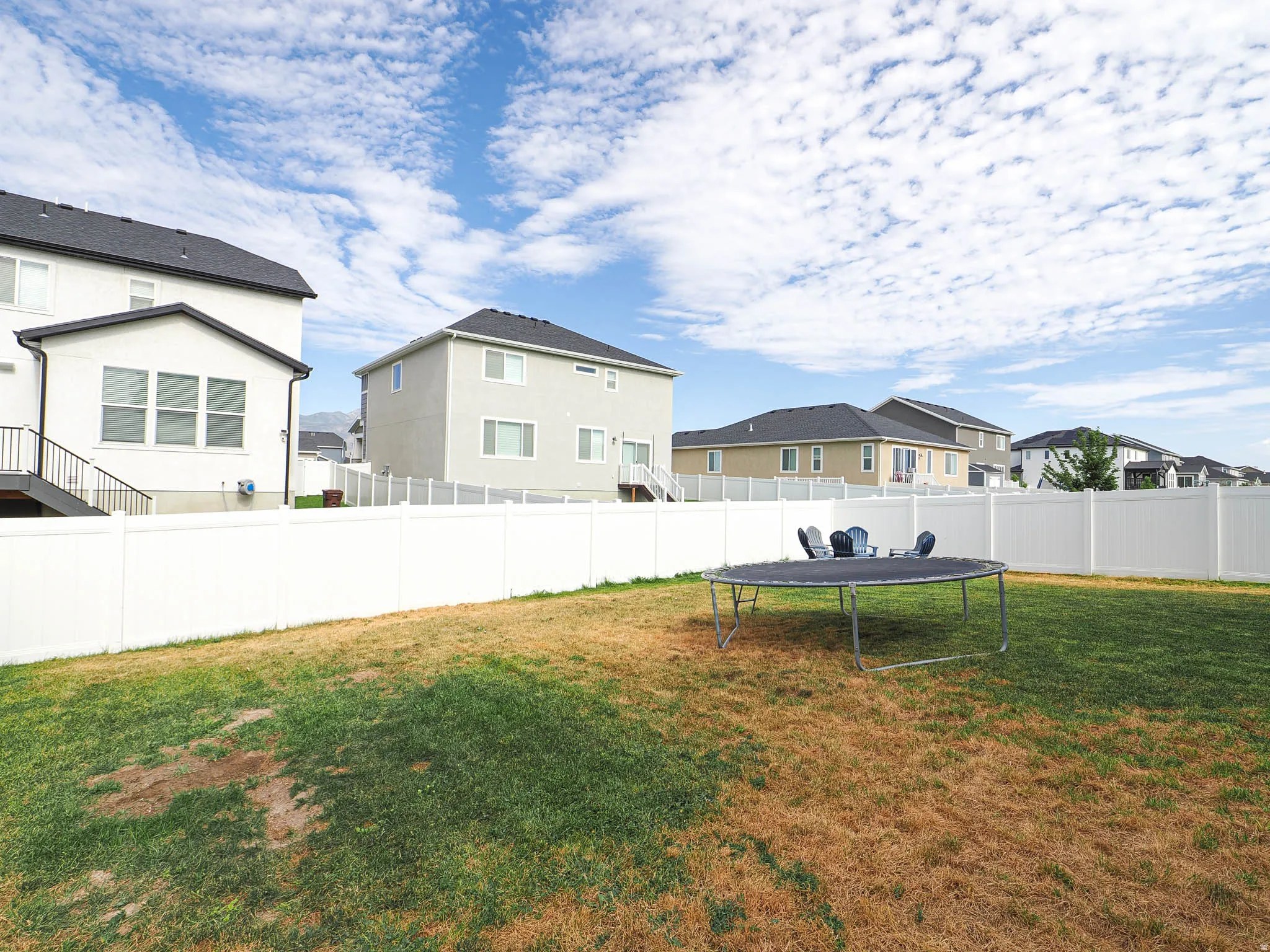 Expansive backyard featuring a white vinyl fence, green lawn, and a light-colored stucco exterior with dark roofing