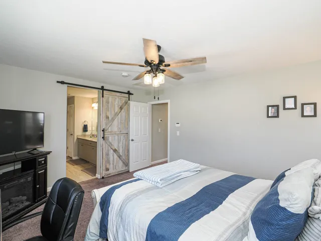 Spacious room featuring a rustic wood-finish barn door, a ceiling fan with integrated lighting, and neutral wall paint