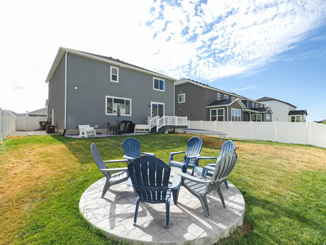 Expansive backyard featuring a circular paver patio, a white vinyl privacy fence, and a two-story exterior with multiple windows