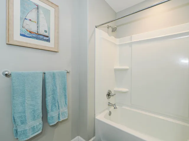 Bathtub with an integrated shower surround featuring a chrome showerhead and faucet