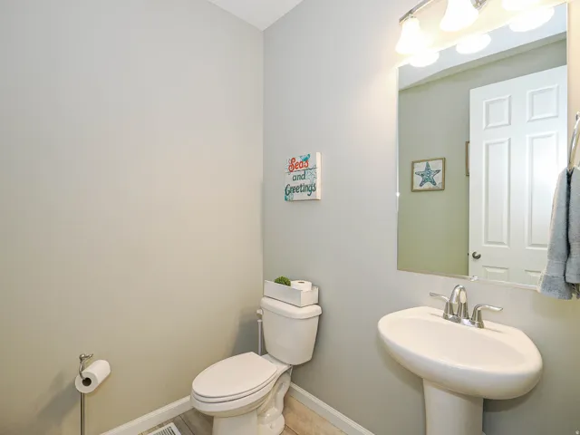Bathroom featuring a pedestal sink with chrome faucet, a white toilet, and a wall-mounted mirror