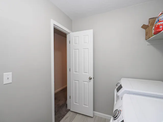 Laundry area featuring light gray walls, wood-finish flooring, white baseboards, and a built-in wall shelf