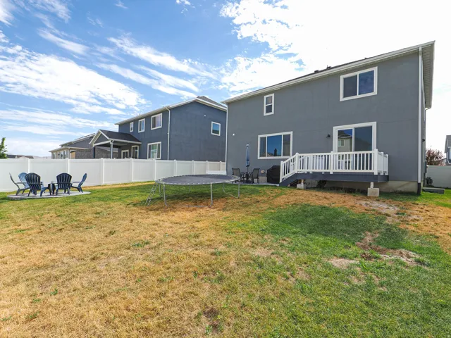 Expansive rear yard featuring a privacy fence, concrete patio, and a deck with white railings