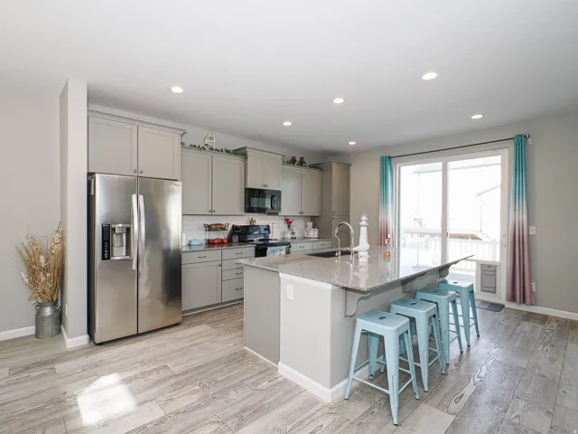 Bright kitchen featuring light gray cabinetry, stainless steel appliances, a large center island with a sink and seating, wood-finish flooring, and a sliding glass door