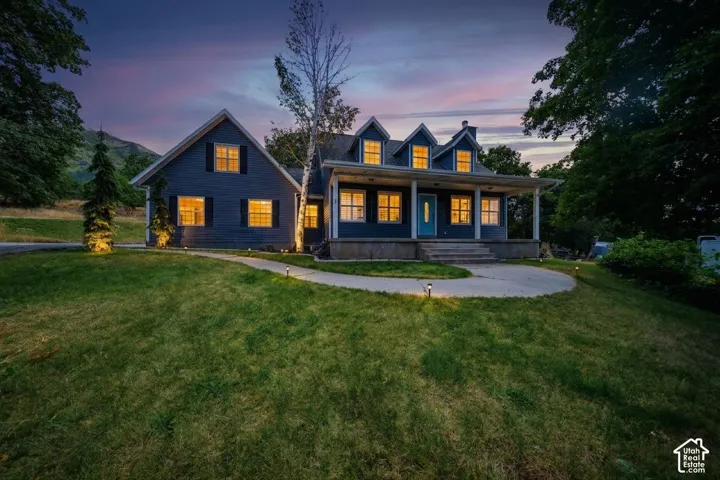 Two-story residence featuring dormer windows, a covered front porch with white columns, dark siding, and a contrasting blue front door