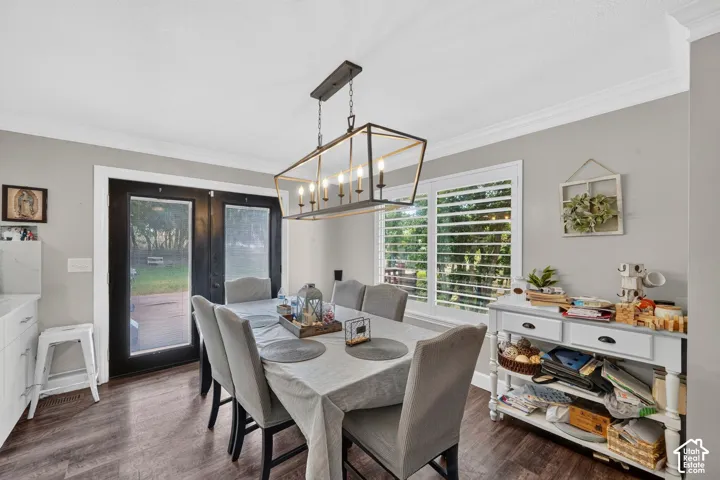 Dining area featuring wood-finish flooring, a modern linear chandelier, crisp white crown molding, and plantation shutters