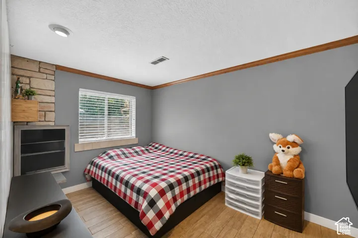 Well-lit room featuring wood-finish flooring, a stone-accented wall, and a window with blinds