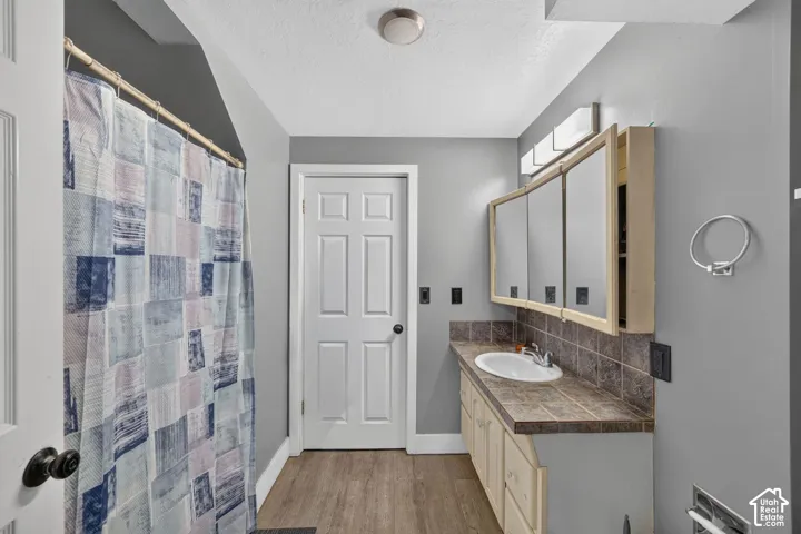 Bathroom featuring a single vanity with a white basin sink, tile countertop, and light wood-finish cabinetry
