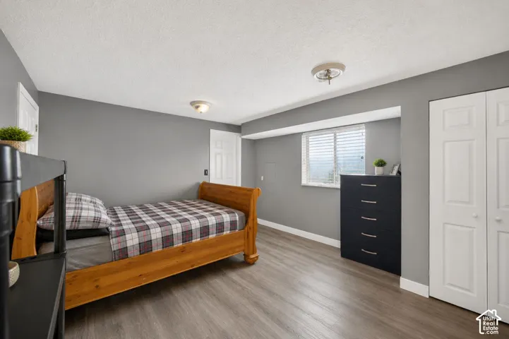 Spacious room featuring wood-finish flooring, neutral gray walls, a window with blinds, and white bi-fold closet doors