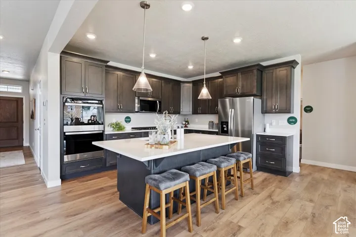 Spacious kitchen featuring wood-finish flooring, dark wood cabinetry, a large center island with a light-colored countertop, stainless steel appliances, and recessed lighting